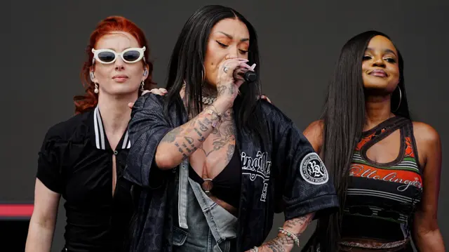 Trio Sugababes perform on stage. Two bandmembers have long brown hair and one has red hair.