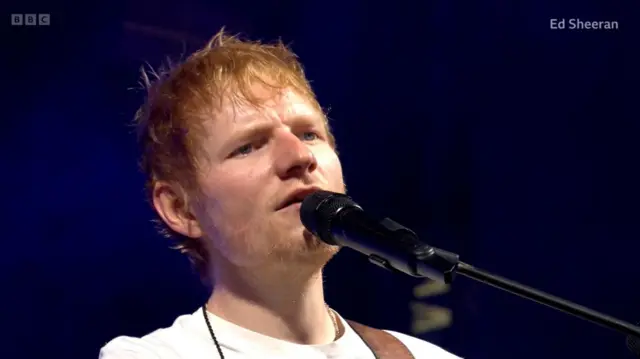 Ed Sheeran close up as he performs on stage in a white t-shirt