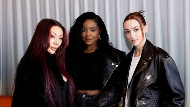 Three women stood in a line next to each other posing for the camera