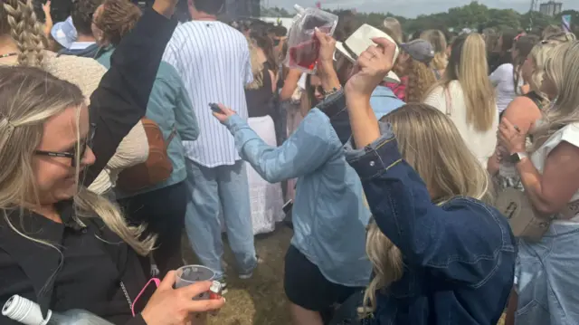 Vicky and a friend dance to the Sugababes. they're in a crowd at a music festival and holding drinks