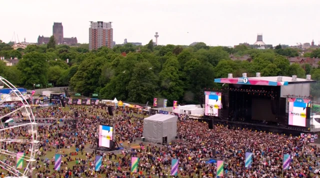 Large crowds stood in front of stage, aerial view.