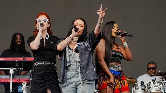 The Sugababes sing into microphones on stage
