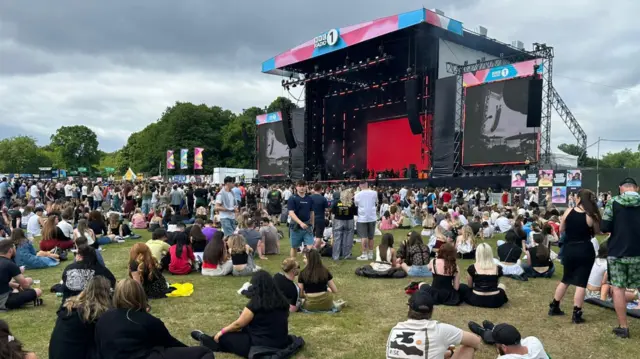 Hundreds of people sit on the grass at a music festival