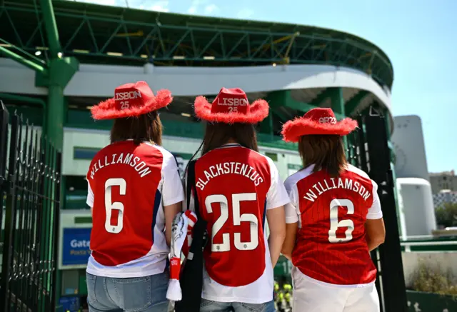 Fans with red cowboy hats and Arsenal shirts stand outside the ground