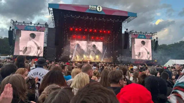 A view of a stage with Mumford and Sons playing, lots of people watching.