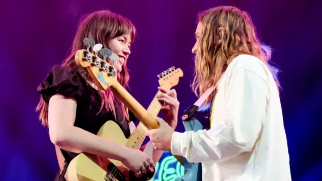 Rhian Teasdale, lead vocalist, and guitarist and Ellis Durand perform on stage together. Teasdale has long brown hair and Durand has long blonde hair. They are both playing guitars.
