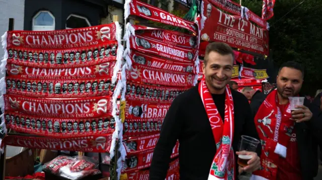 Fans drink pints of beer by a displays of red scarves reading the words 'Champions'