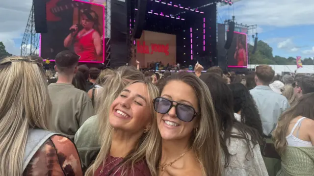 The two Izzys smile at the camera. The stage where Lola Young is performing is in the backround.