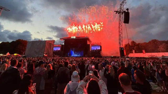 Crowd looking at fireworks above stage.