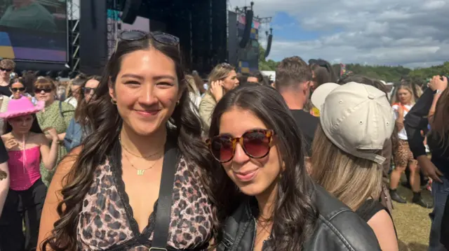 Ella, wearing a cheetah print top, with Maria, who is wearing sunglasses and a leather jacket. Both smile at the camera as they're in the crowd