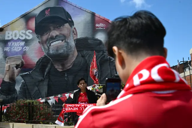 Liverpool fan stands facing a huge mural of former Liverpool manager Jurgen Klopp on the gable end of a building