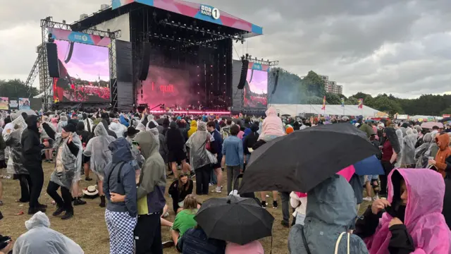 Festival-goers hold umbrealls and wear anoraks amid  a downpour at the Main Stage