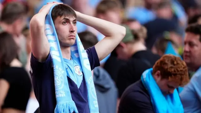 A downbeat Manchester City fan with their hands on their head