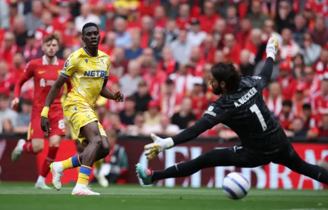 Crystal Palace's Ismaila Sarr, wearing all yellow, scores past Liverpool's diving goalkeeper Alisson Becker.