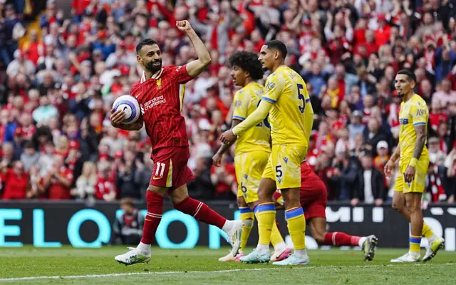 Mo Salah wheels away in celebration after scoring for Liverpool. His left fist is raised and he carries the match ball in his right hand
