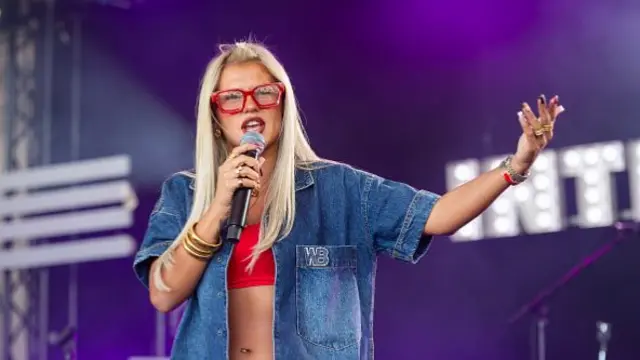 Skye Newman sings on stage with red glasses.