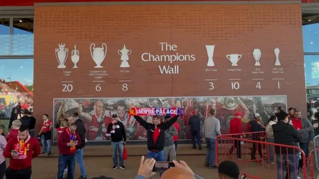A fan holds a scarf aloft below Liverpool's champions wall