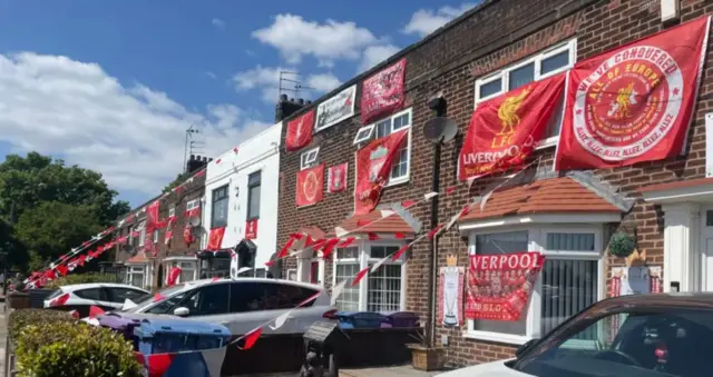 A row of terraced houses draped in red and white Liverpool flags, bunting and banners