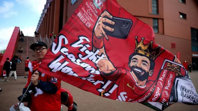 A fan holds a flag showing Mo Salah's iconic selfie