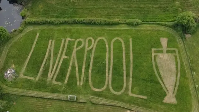 A birdseye view of the words Liverpool cut into a lawn next to a Premier League tropphy