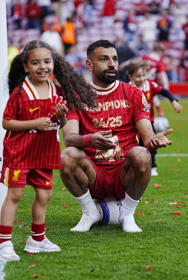 Salah sits on a ball as his daughter plays around