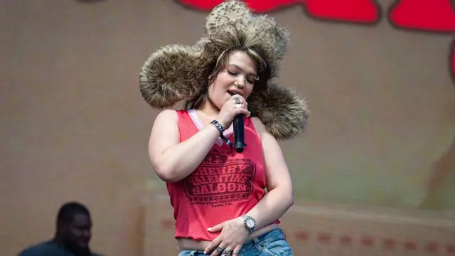 Lola Young on stage, wearing big fur hat.