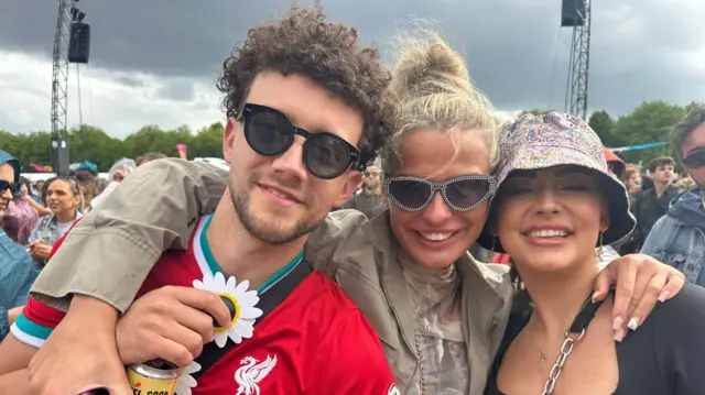Jacob, Niamh and Belle pictured with arms around each other. Jacob and Niamh are wearing sunglasses, while Belle is donning a bucket hat. The skies are grey in the background