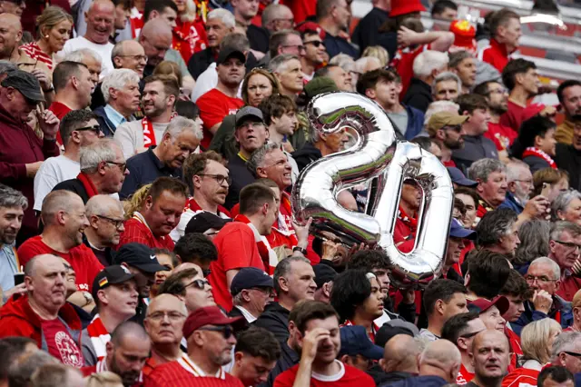 Stand full of Liverpool fans, mostly wearing red. Large silver balloons, illustrating the number 20 in reference to the number of top-flight league titles won by the Reds, are held aloft