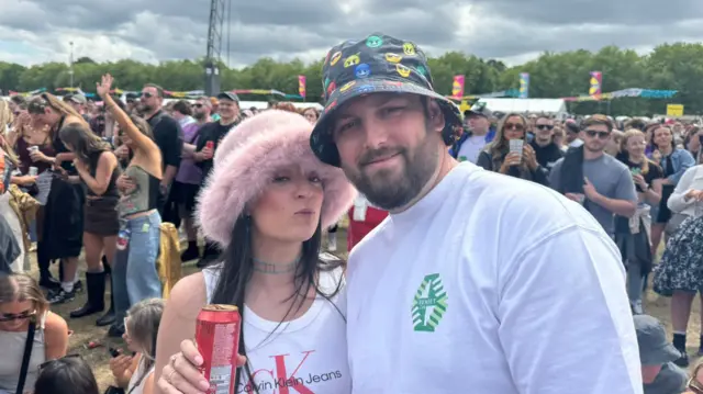 Jade, wearing a pink , fluffy bucket hat, with Jamie, who is wearing a black hat with the devil emoji on it in different colours