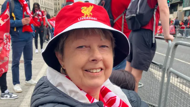 Heather Greenhalgh wearing a Liverpool hat and scarf sitting on a foldable chair to wait for the open-top parade