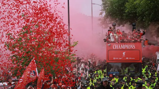 Red confetti thrown in the air and red flares as the team show the trophy from the top of the open-top bus
