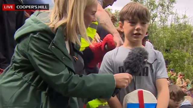 BBC reporter in green jacket interviews winner of under 11s uphill cheese race