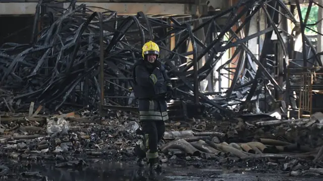 A firefighter in Kharkiv puts out the flames of a charred building.