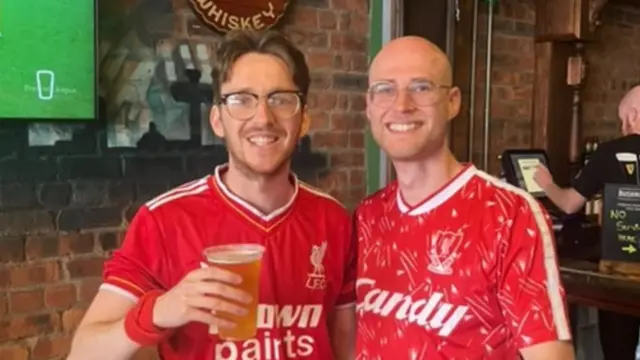 Harry and Oli in Liverpool shirts smiling at the camera