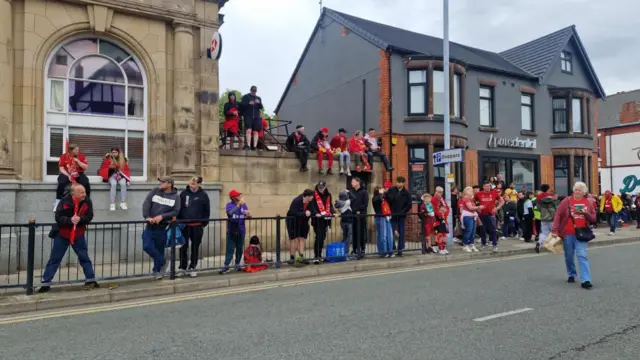 Crowds stood along the pavement and sitting on the wall along Allerton Road