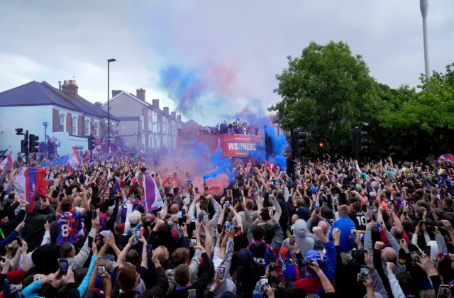 Red and blue smoke and the victory bus surrounded by crowds