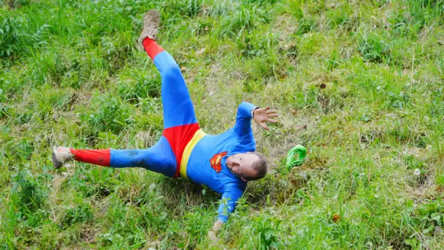 A man dressed as superman is tumbling down the hill on his back, his arms and legs flying up.