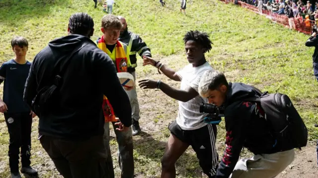 Image shows iShowSpeed talking to winner of the men's race at the bottom of Cooper's Hill. He is wearing a white t-shirt and black adidas bottoms.