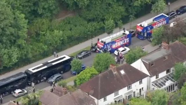 Four buses, two of which are Palace buses with the word winners on the side, parked in a row on a street
