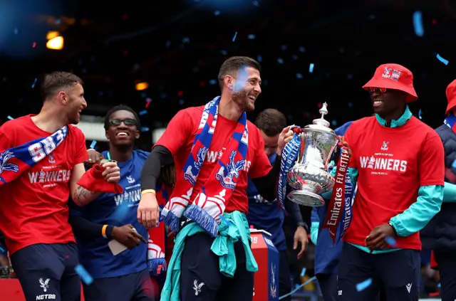 A group of men smile while two at the front hold a large silver trophy