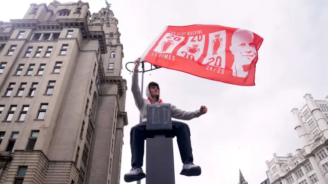Liverpool fan waving a flag sits on top of a traffic camera