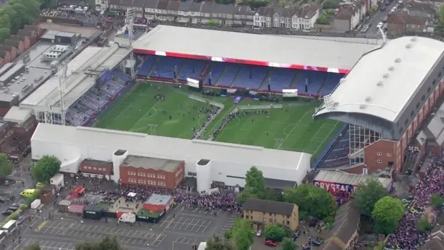 Birds eye view of the stadium with people around it and a stage set up inside with barriers