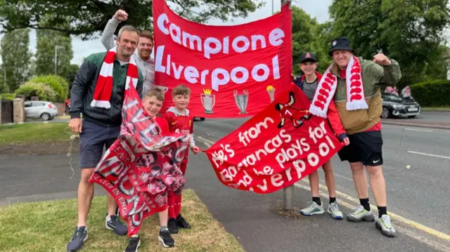 A group of Liverpool fans holding a banner that says Campione Liverpool
