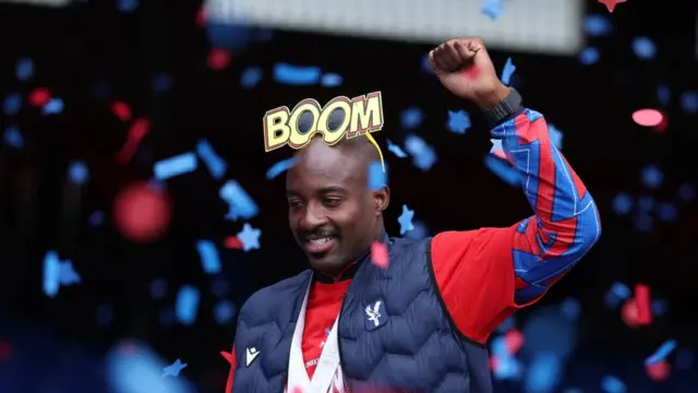 Mateta headshot as he holds one fist in the air and wears large novelty sunglasses that say boom