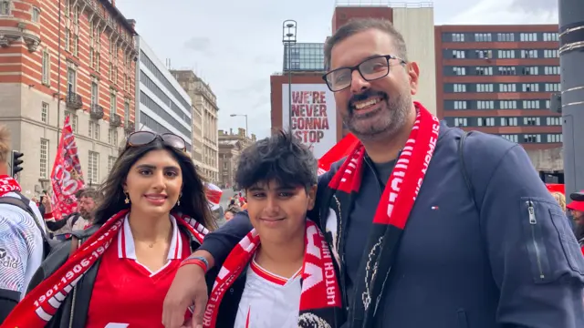 Liverpool fans Ajay, Jaiya and Sundeep wearing Liverpool scarves and tops as they wait for the open-top bus parade in Liverpool city centre