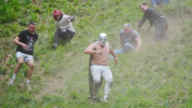 Five men are making their way down the hill. The man in the centre is wearing a wrestling mask and knee pads.