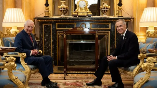 King Charles and Mark Carney sitting opposite each other at Buckingham Palace, both smiling at the camera