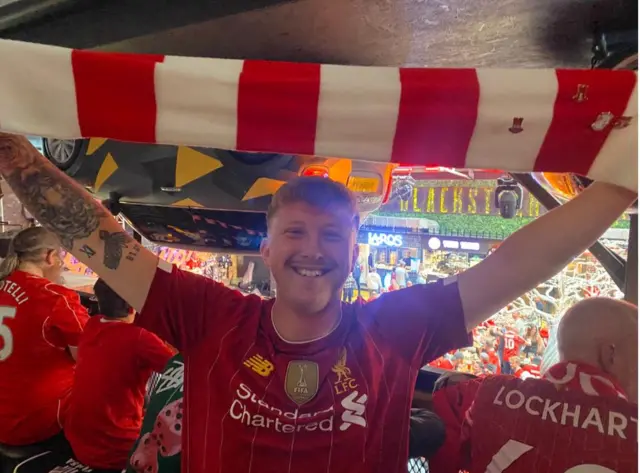 Man wearing Liverpool football shirt and holding flag in the air