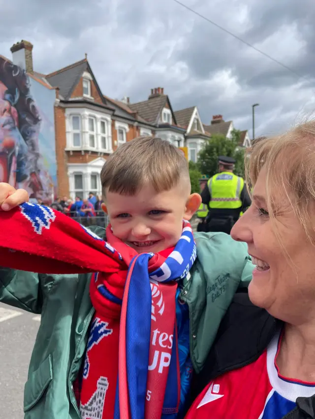 A small boy being held by older woman in Crystal Palace football shirts