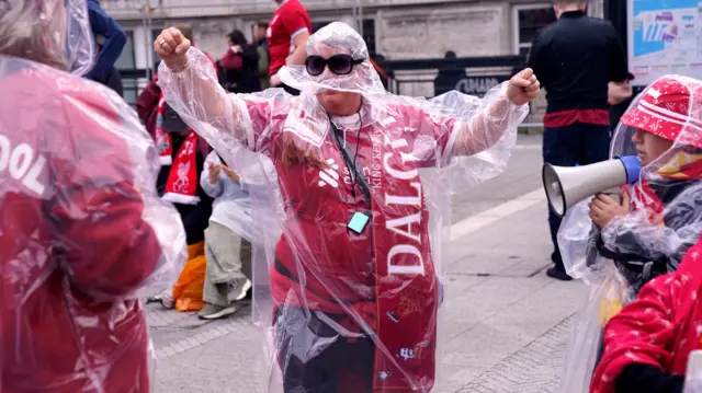 Woman wears a plastic poncho over her LIverpool shirt and red scarf